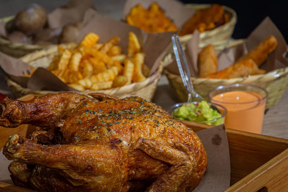 Poulet rôti doré posé sur une table en bois, entouré de plats d'accompagnement : pommes de terre, légumes rôtis et salade verte