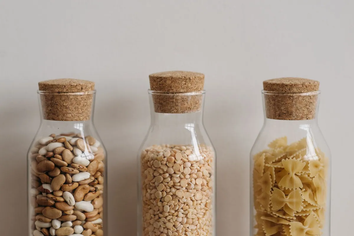 Bocaux en verre alignés contenant des lentilles vertes, des lentilles corail, des pois chiches et des haricots blancs secs