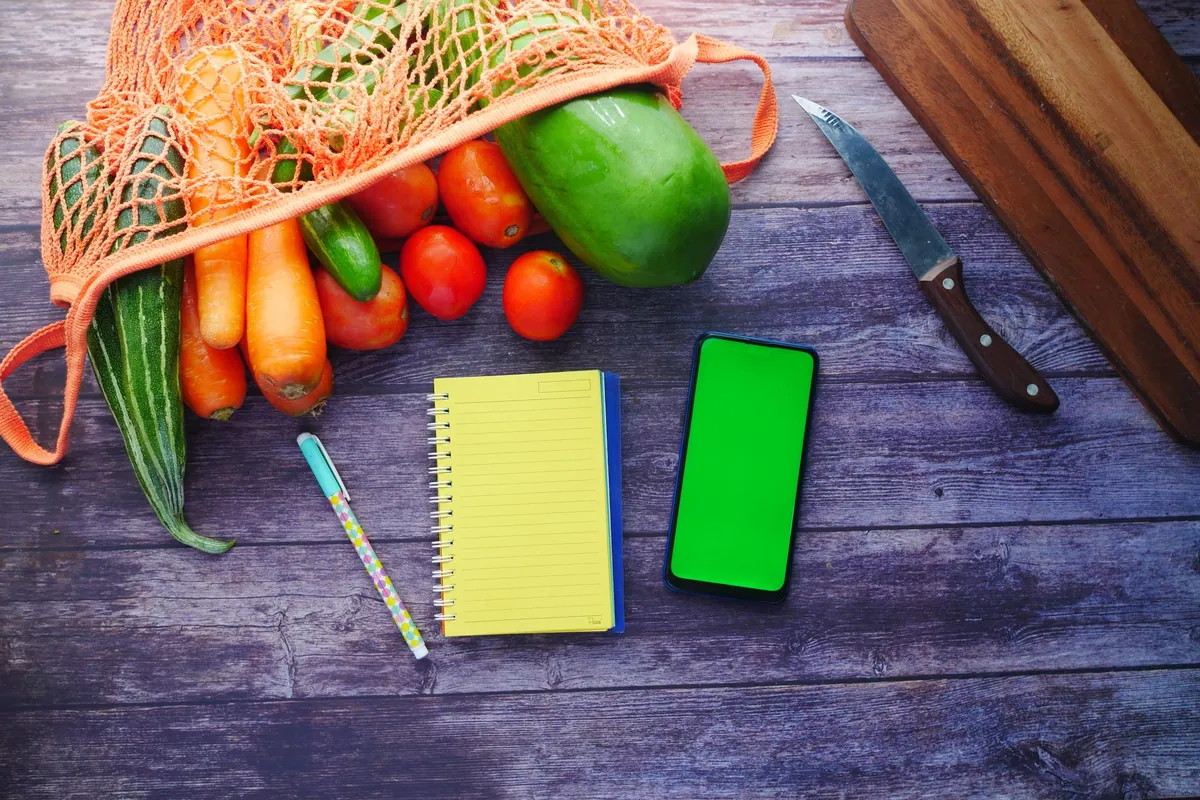 Liste de courses manuscrite posée à côté de légumes frais, vue de dessus