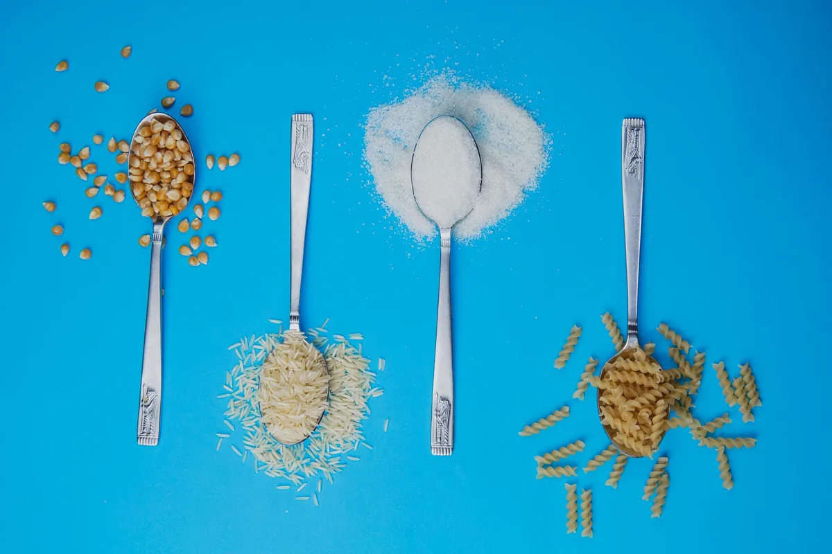 Balance de cuisine et petits bols contenant des portions mesurées de riz, de pâtes et de lentilles sur un plan de travail clair