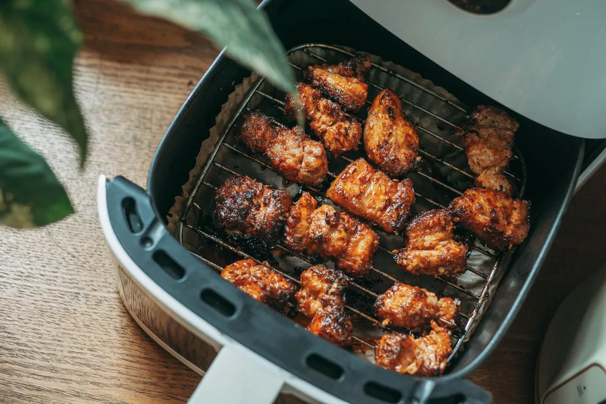 Panier d'air fryer ouvert sur un plan de travail, garni de morceaux de légumes et de poulet dorés en une seule couche