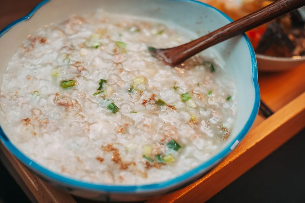 Bol de congee crémeux garni de poulet effiloché, oignons nouveaux et gingembre râpé